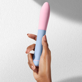 A hand holding the light blue and pink ffix Bullet XL against a textured white wall.