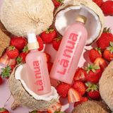 A lifestyle image showing a bottle of La Nua's Strawberry Coconut lube with fresh strawberries and coconut pieces.