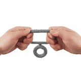 A person's hand holding up a gray silicone double cock ring, showcasing its two connected loops.